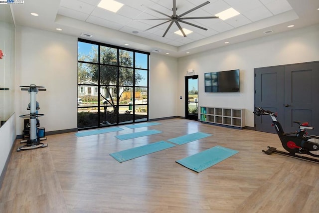 workout room featuring a towering ceiling, light hardwood / wood-style floors, a raised ceiling, and ceiling fan