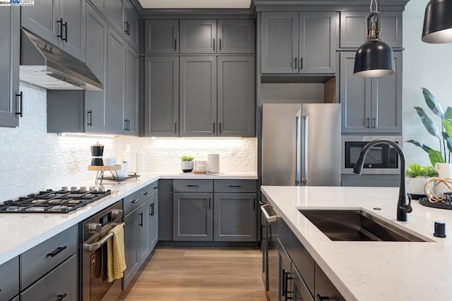 kitchen with sink, light stone counters, backsplash, appliances with stainless steel finishes, and light wood-type flooring