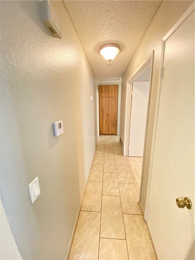 corridor featuring a textured ceiling and light tile patterned floors