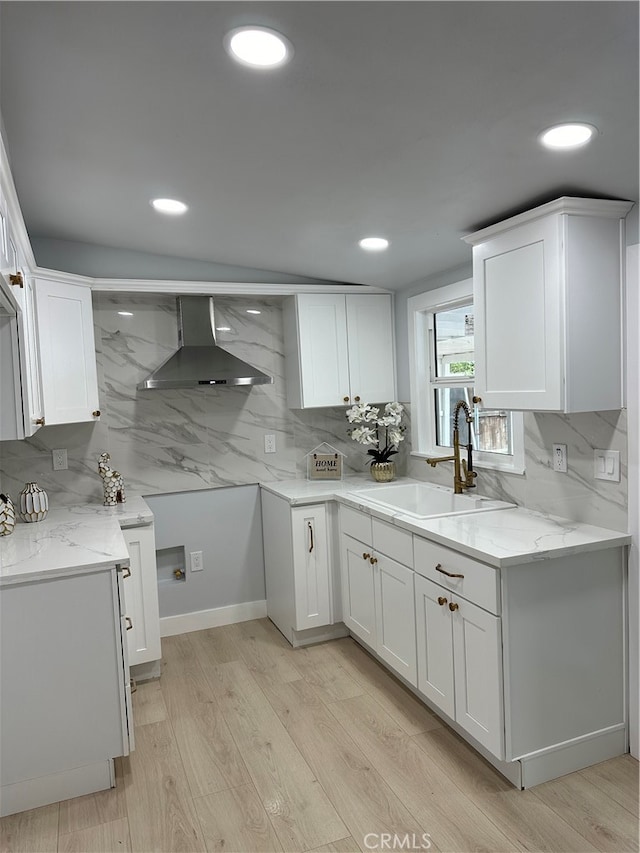 kitchen featuring light hardwood / wood-style floors, white cabinetry, sink, and wall chimney range hood