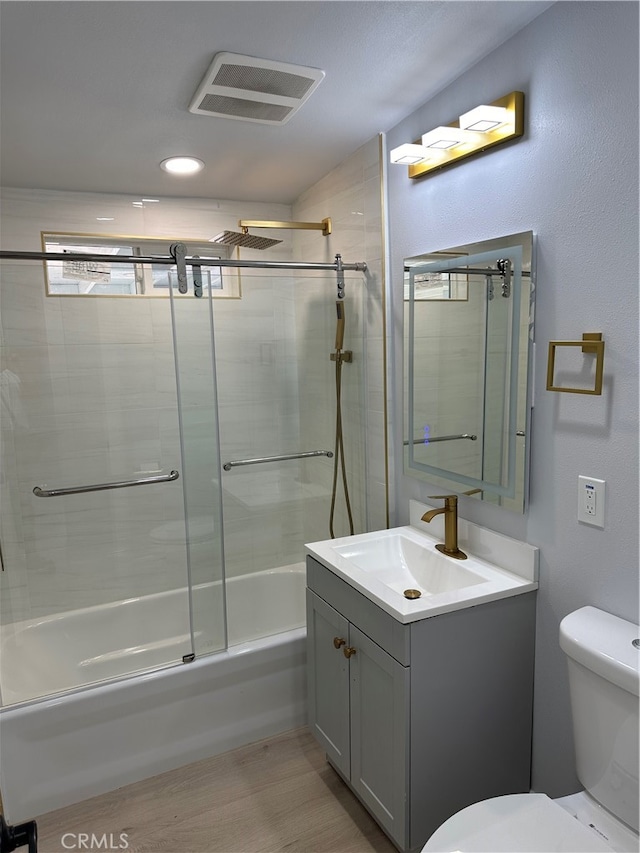 full bathroom with wood-type flooring, shower / bath combination with glass door, vanity, and toilet