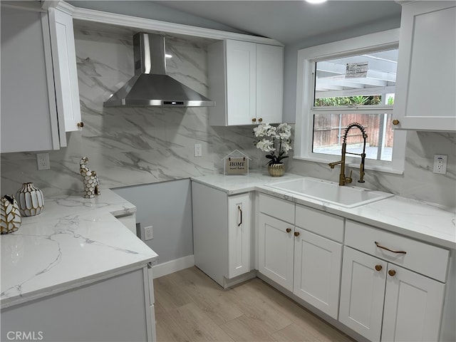 kitchen with sink, tasteful backsplash, wall chimney exhaust hood, white cabinetry, and light stone countertops