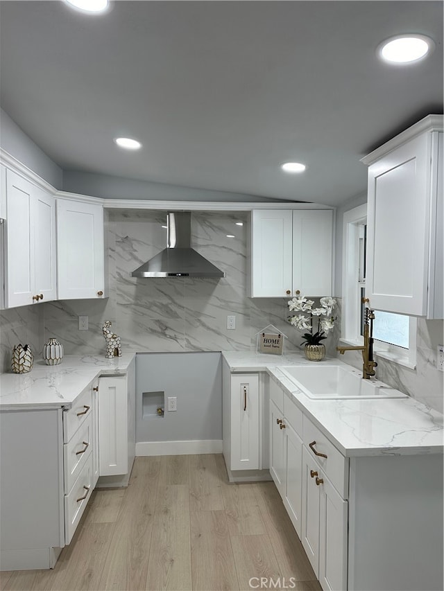 kitchen with wall chimney exhaust hood, white cabinetry, and sink