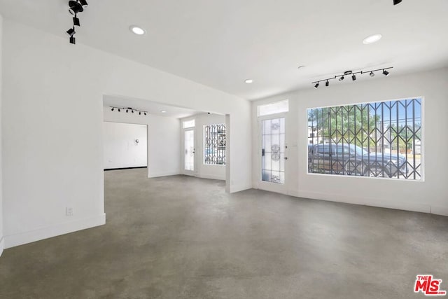 unfurnished living room featuring track lighting, concrete floors, and a wealth of natural light