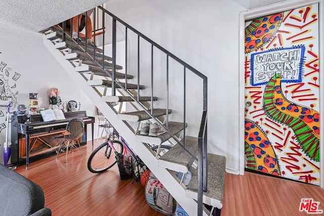 staircase with a textured ceiling and wood-type flooring