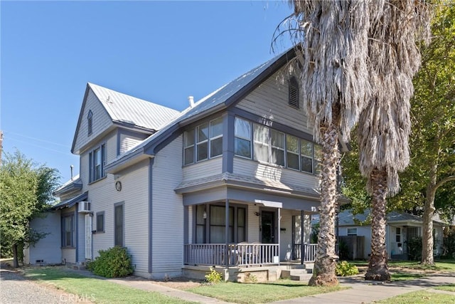 view of front of home featuring a wall mounted AC, covered porch, and a front yard