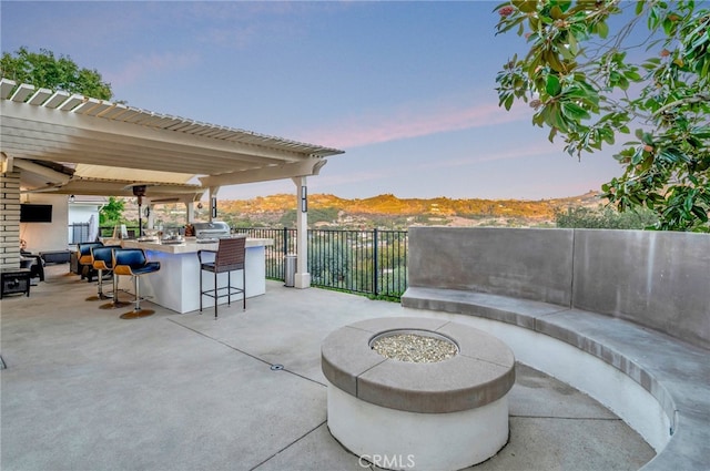 patio terrace at dusk with an outdoor bar, a mountain view, a grill, a fire pit, and ceiling fan