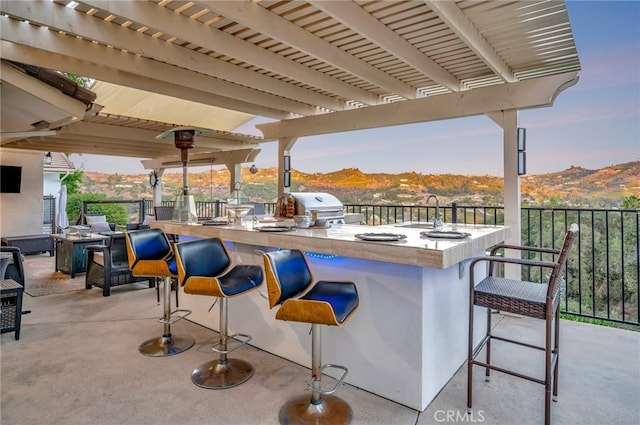 patio terrace at dusk featuring a grill, an outdoor wet bar, a mountain view, and an outdoor kitchen