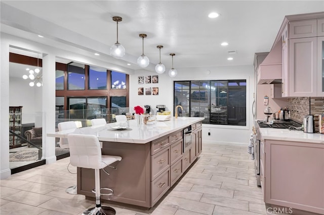 kitchen with an island with sink, backsplash, pendant lighting, gas range, and custom exhaust hood