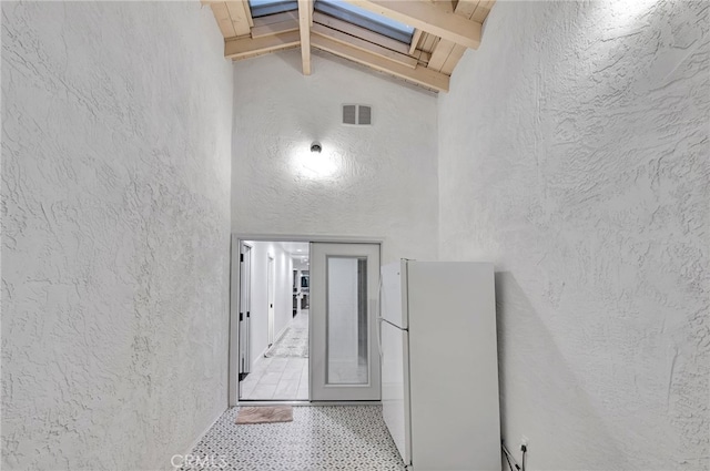 corridor with beam ceiling, a skylight, and high vaulted ceiling