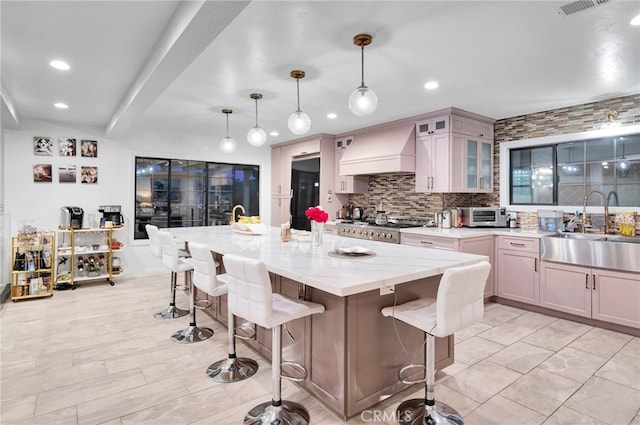 kitchen featuring backsplash, a breakfast bar area, decorative light fixtures, premium range hood, and sink