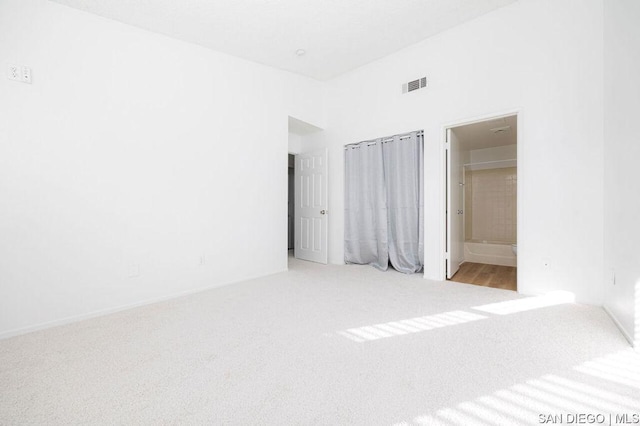 unfurnished bedroom featuring ensuite bathroom, light colored carpet, and a towering ceiling