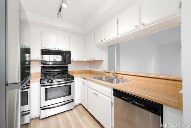 kitchen with appliances with stainless steel finishes, light wood-type flooring, track lighting, white cabinets, and sink