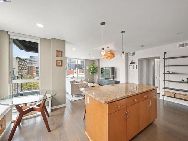 kitchen featuring dark wood-type flooring, a kitchen island, pendant lighting, and light stone counters