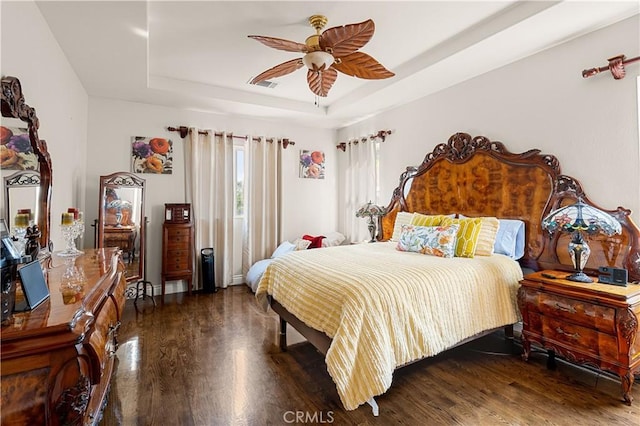 bedroom with a raised ceiling, dark hardwood / wood-style flooring, and ceiling fan