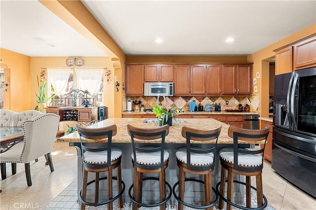 kitchen featuring tasteful backsplash, a breakfast bar, an island with sink, and black fridge