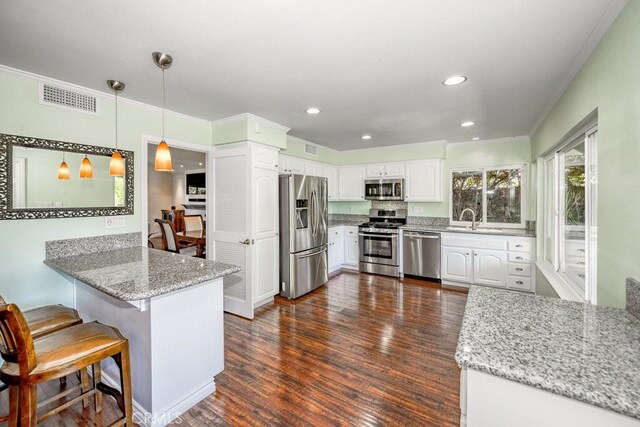 kitchen featuring kitchen peninsula, stainless steel appliances, pendant lighting, dark hardwood / wood-style floors, and white cabinetry