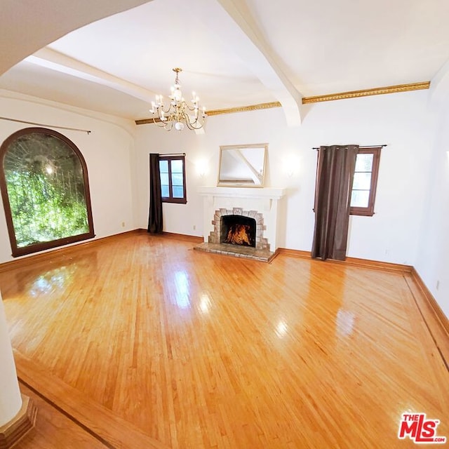 unfurnished living room featuring a stone fireplace, hardwood / wood-style flooring, plenty of natural light, and a chandelier