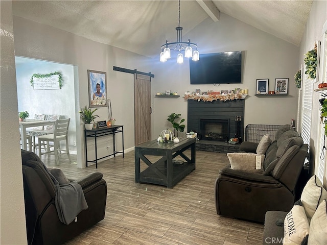 living room featuring hardwood / wood-style flooring, lofted ceiling with beams, a notable chandelier, a fireplace, and a barn door