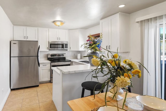 kitchen featuring light tile patterned flooring, a breakfast bar area, white cabinets, kitchen peninsula, and stainless steel appliances