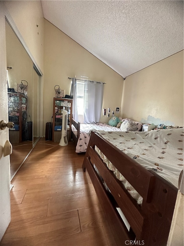 bedroom with wood-type flooring, a textured ceiling, a closet, and vaulted ceiling