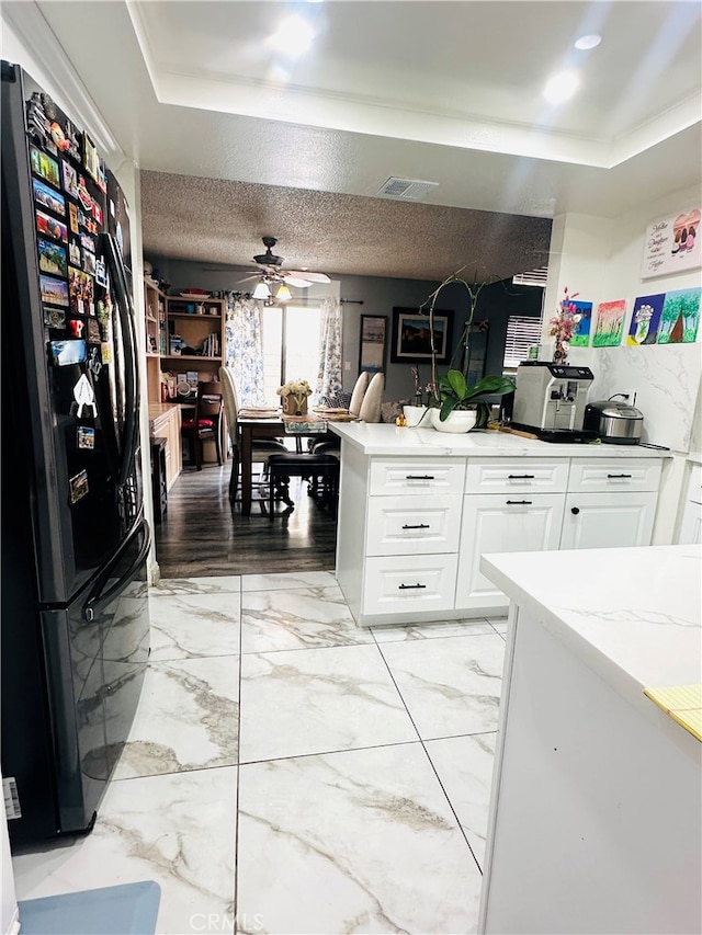 kitchen featuring ceiling fan, a textured ceiling, white cabinetry, light stone countertops, and black refrigerator