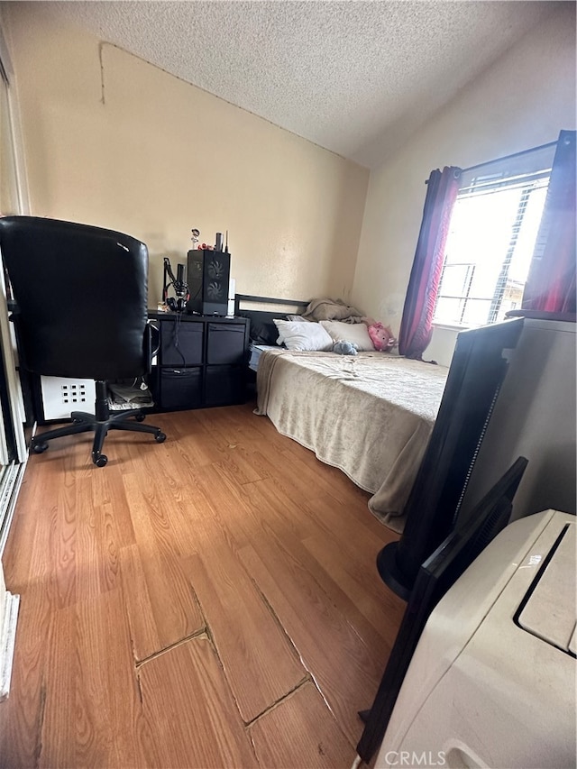 bedroom featuring lofted ceiling, light hardwood / wood-style floors, and a textured ceiling