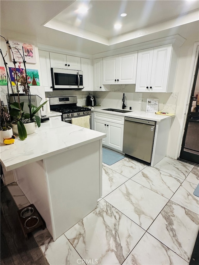 kitchen with a tray ceiling, sink, white cabinetry, kitchen peninsula, and stainless steel appliances