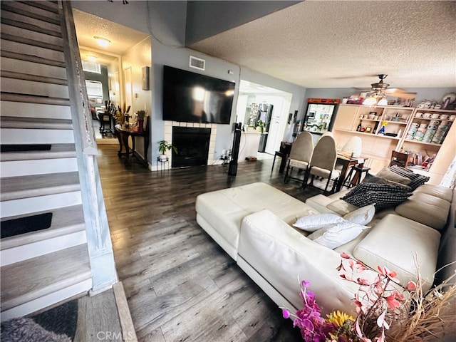 living room featuring a textured ceiling, a tiled fireplace, ceiling fan, and hardwood / wood-style flooring