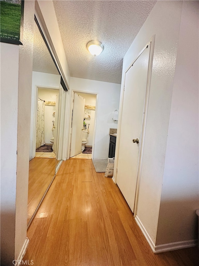 hall with light wood-type flooring and a textured ceiling