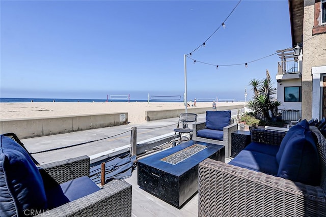 view of patio featuring a view of the beach, a water view, and an outdoor living space with a fire pit