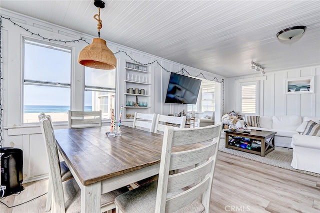 dining area featuring a water view, a healthy amount of sunlight, built in shelves, and light hardwood / wood-style floors