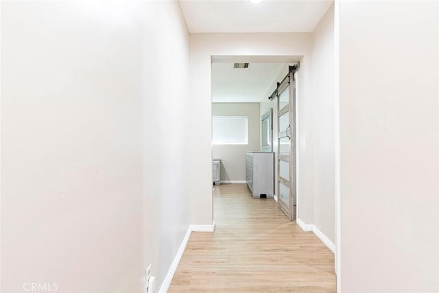 corridor with a barn door and light hardwood / wood-style flooring