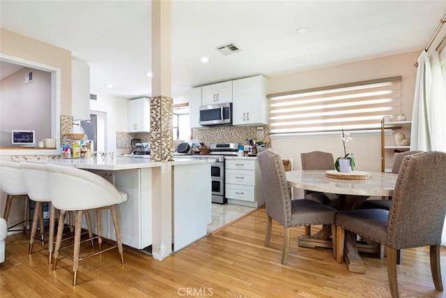 kitchen featuring kitchen peninsula, stainless steel appliances, light hardwood / wood-style flooring, white cabinetry, and a breakfast bar area