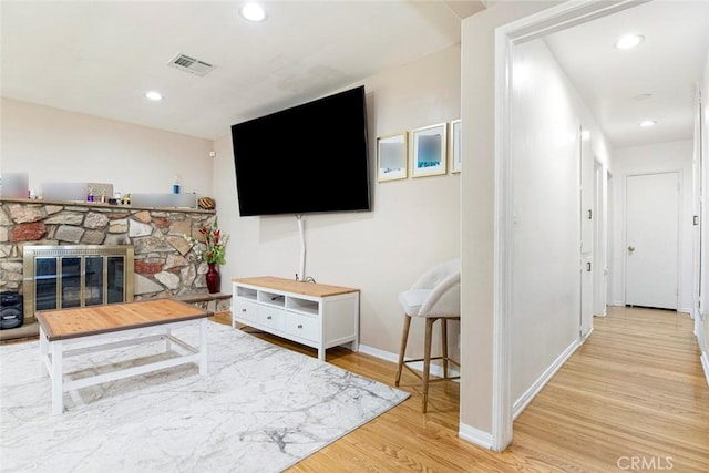 living room featuring a stone fireplace and light wood-type flooring