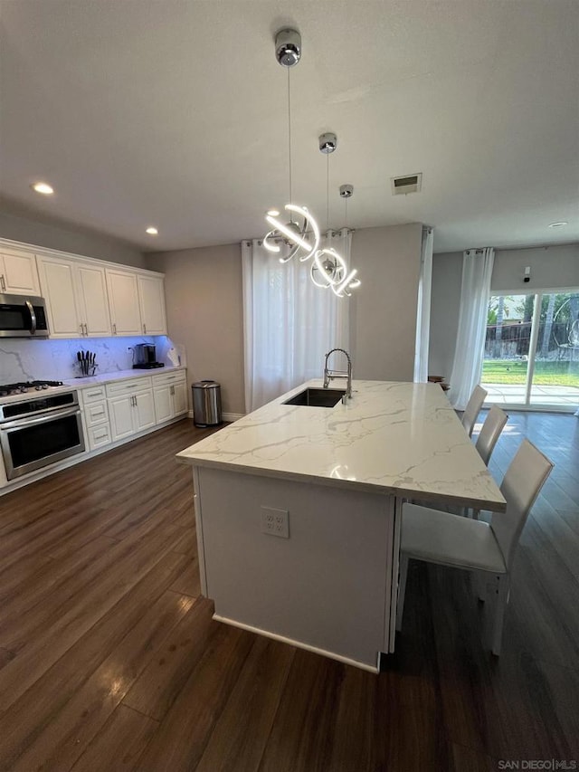 kitchen featuring pendant lighting, white cabinets, sink, a center island with sink, and stove