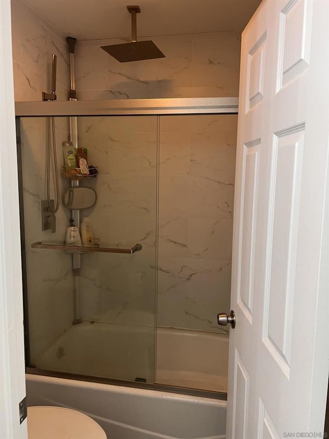 bathroom featuring toilet and bath / shower combo with glass door