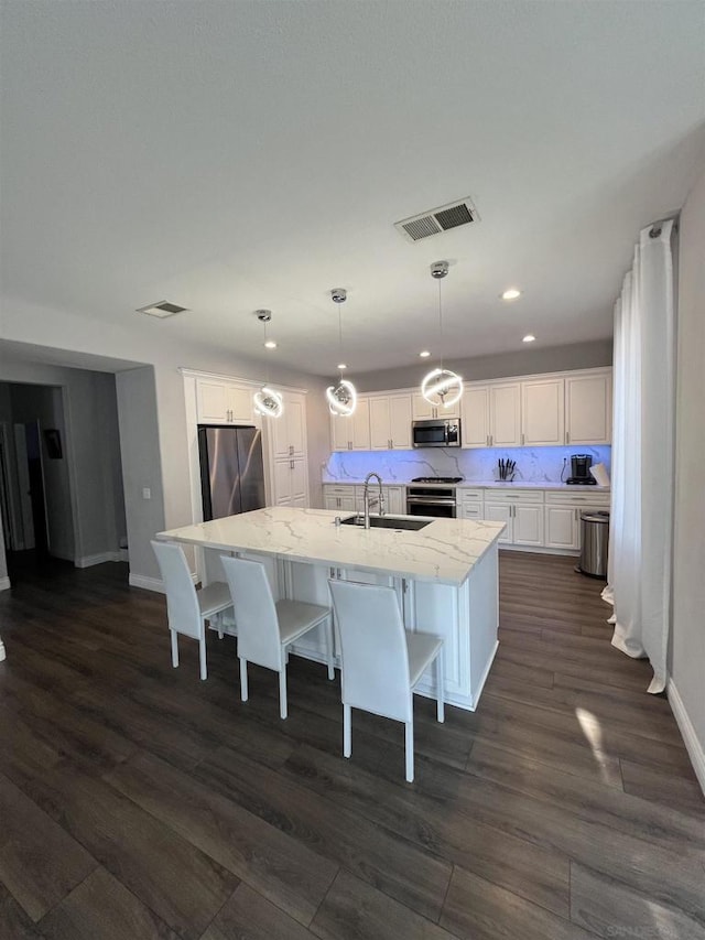 kitchen featuring white cabinetry, a center island with sink, appliances with stainless steel finishes, hanging light fixtures, and sink