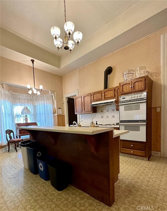 kitchen with a kitchen island, double oven, pendant lighting, and a notable chandelier