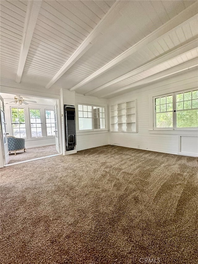 unfurnished living room featuring ceiling fan, beam ceiling, carpet flooring, and a healthy amount of sunlight