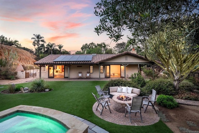 back house at dusk with a lawn, an outdoor living space with a fire pit, a patio, and solar panels