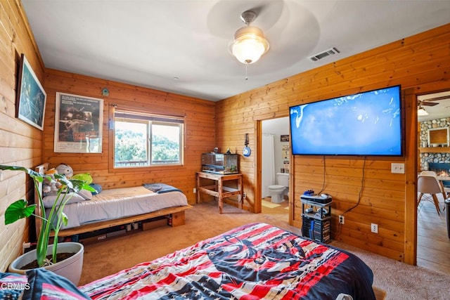 bedroom with ensuite bathroom, ceiling fan, carpet, and wooden walls