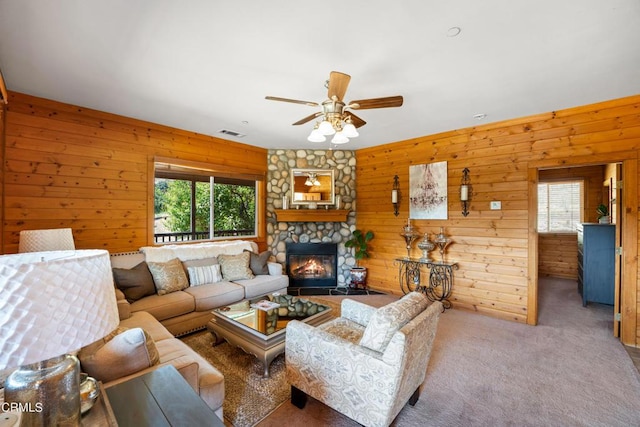 living room with ceiling fan, light colored carpet, a stone fireplace, and wooden walls