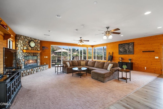 living room with ceiling fan, wood walls, a stone fireplace, and light wood-type flooring