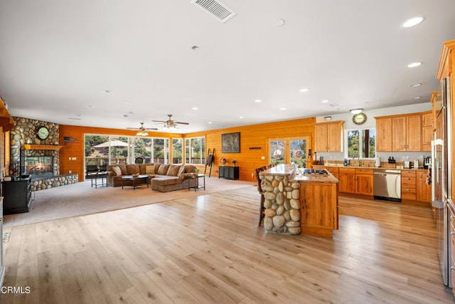 kitchen featuring ceiling fan, a stone fireplace, stainless steel appliances, and light hardwood / wood-style flooring