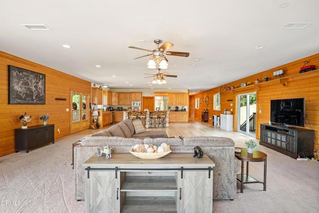 carpeted living room featuring ceiling fan and wooden walls