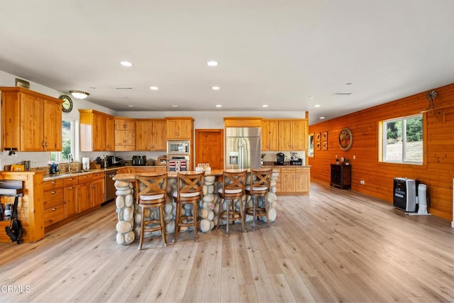 kitchen featuring wooden walls, appliances with stainless steel finishes, light wood-type flooring, a kitchen island, and sink