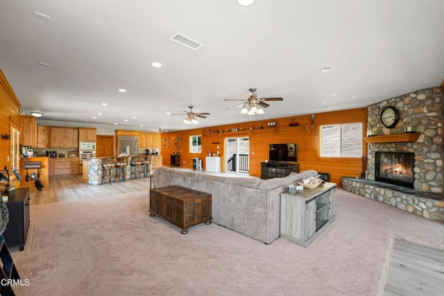 living room featuring ceiling fan, light hardwood / wood-style floors, wood walls, and a fireplace