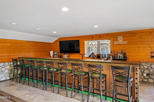 bar featuring light tile patterned floors, vaulted ceiling, and wood walls