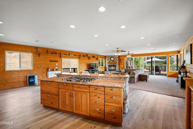 kitchen featuring ceiling fan, stainless steel gas cooktop, light wood-type flooring, and wood walls